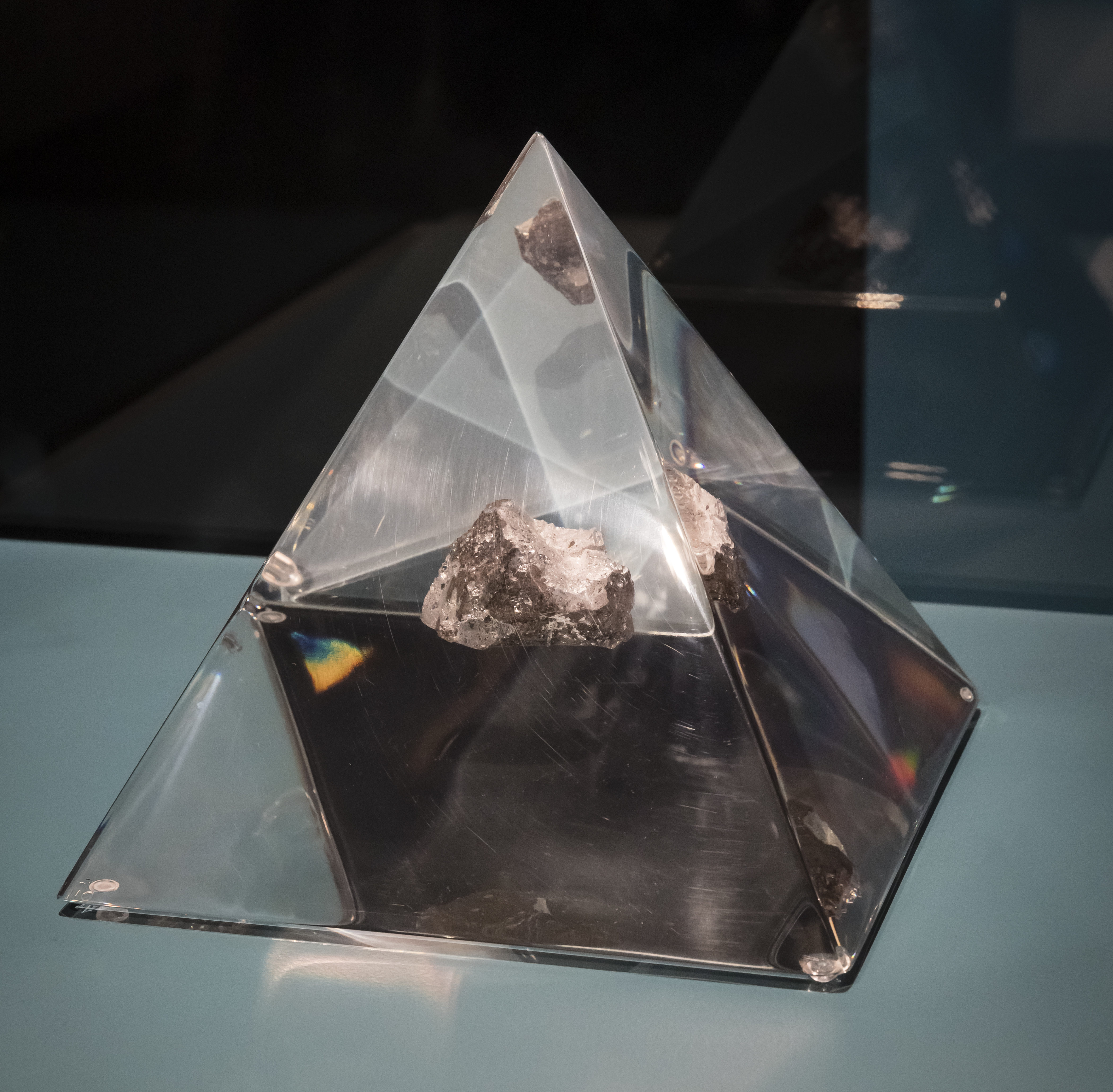 A small piece of rock, appoximately 3cm in diameter, encased in a perspex pyramid.